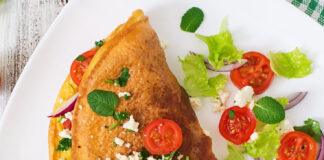 Omelet with tomatoes, parsley and feta cheese on white plate.
