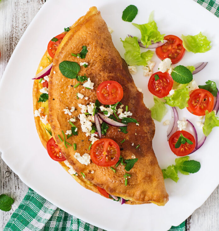 Omelet with tomatoes, parsley and feta cheese on white plate.