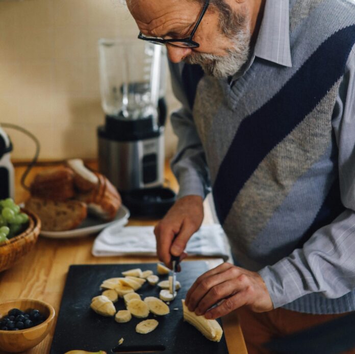 Elderly Man Slicing a Banana on a Chopping Board